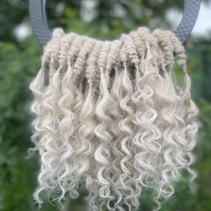 May include: A bundle of light blonde curly hair extensions. The hair is arranged in a circle and is ready to be used for braiding or weaving.