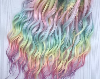 Puede incluir: Un conjunto de rastas de colores arcoíris pastel, con tonos de rosa, amarillo, verde y azul. El cabello ondulado está atado con una cinta de arcoíris. Las rastas tienen un aspecto suave y texturizado.