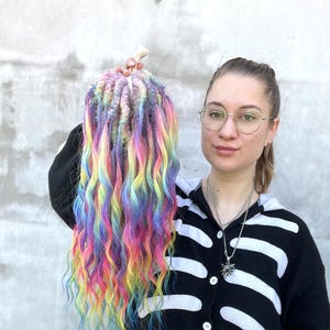 Może przedstawiać: Zestaw kolorowych, falowanych syntetycznych dredów. Dredy są połączeniem różowego, niebieskiego, żółtego i zielonego.