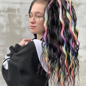 May include: A person with long, black wavy hair with colourful streaks. The hair is pulled back into a ponytail.