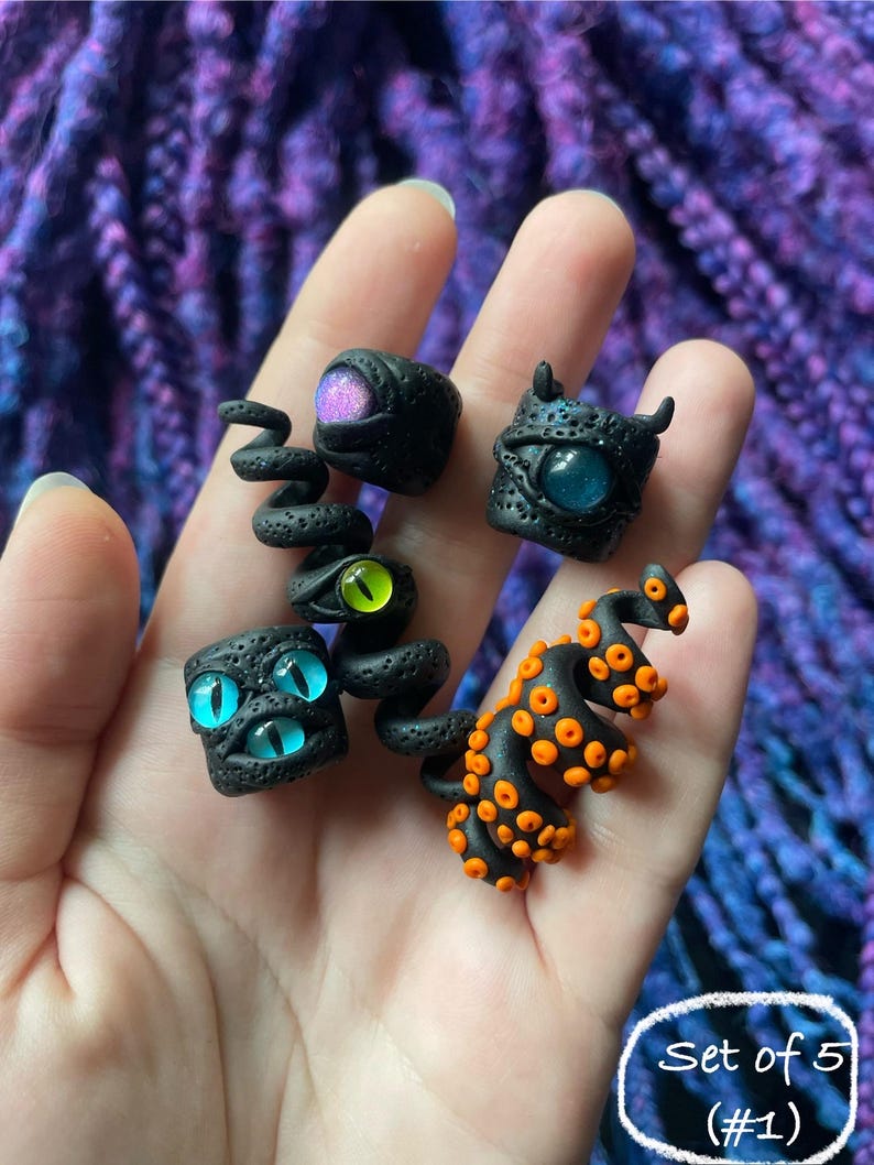 May include: A set of five black polymer clay rings with colorful eye designs. The rings feature various eye colors, including purple, blue, and green, and one ring has orange tentacles. The text "Set of 5 (#1)" is in a white circle.