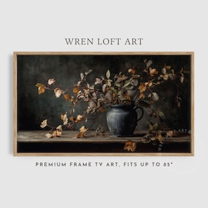 Puede incluir: Una obra de arte enmarcada que presenta una naturaleza muerta con un jarrón azul oscuro lleno de ramas y hojas de otoño. La obra de arte está sobre un fondo oscuro. El texto "WREN LOFT ART" y "PREMIUM FRAME TV ART, FITS UP TO 85" son visibles.