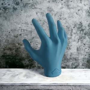 Könnte beinhalten: Ein blaues, 3D-gedrucktes Handmodell mit ausgestreckten Fingern, das auf einer grauen Oberfläche liegt.