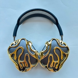 May include: Over-ear headphones with a black headband and gold-colored earcups. The earcups have a unique, organic design with a textured surface.