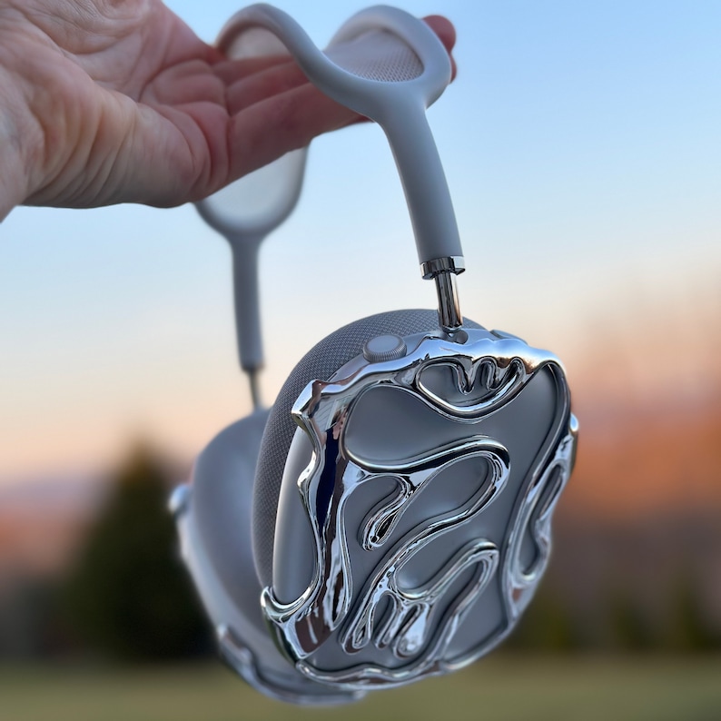 May include: White headphones with a silver, textured, abstract design on the earcups. The headphones have a silver headband with a mesh design.