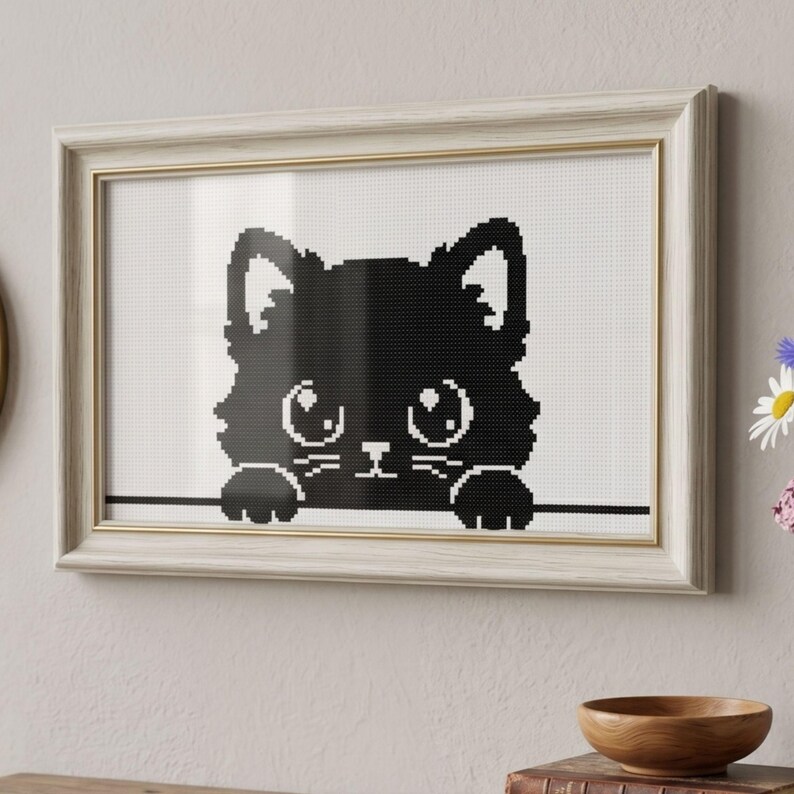 May include: Framed cross-stitch art featuring a black cat silhouette with large eyes and paws. The artwork is set against a white background and framed in a light wood frame with a gold inner edge. A charming piece for cat lovers.