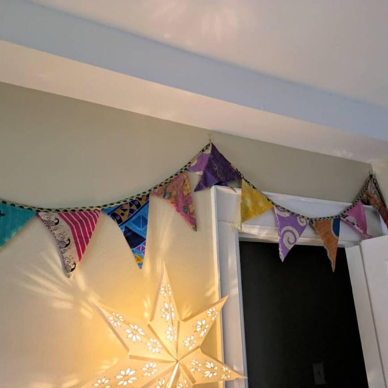 May include: A colorful fabric banner of triangular flags strung across a wall. The flags are various colors and patterns, including pink, blue, and yellow. A star-shaped light fixture is visible below the banner.