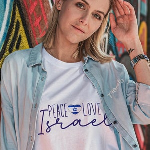 May include: A white t-shirt with a blue and white heart featuring the Israeli flag and the text "Peace Love Israel" in blue lettering.