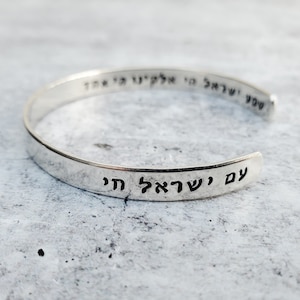 May include: Silver bangle bracelet engraved with the Hebrew phrase "With God, all things are possible".