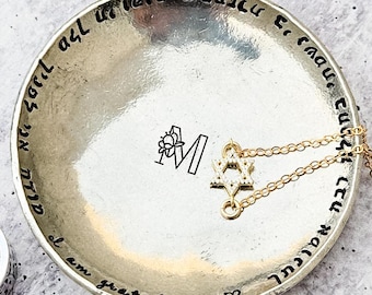 May include: A silver trinket dish with a Hebrew inscription around the edge. The inscription reads "I am grateful" in English. The dish has a small star of David charm with rhinestones and a letter "M" with a flower design inside.
