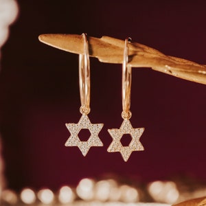 May include: A pair of gold hoop earrings with a dangling star of David charm. Each star is encrusted with small, clear cubic zirconia stones.
