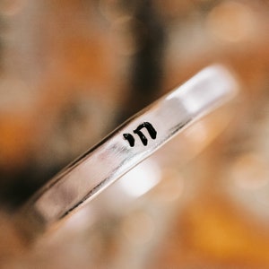 May include: A silver ring with the Hebrew word "mem" engraved on it.