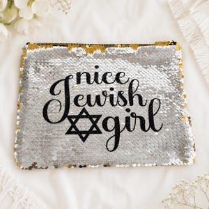 May include: A rectangular pouch covered in shimmering silver sequins featuring the black text "nice Jewish girl" with a black Star of David symbol integrated into the lettering. The pouch has a black zipper closure along the top edge.