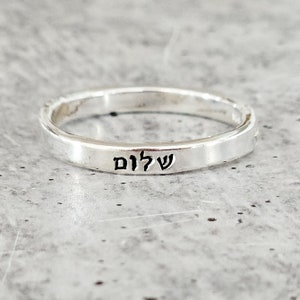 May include: A silver ring with the Hebrew word "Shalom" engraved on it.