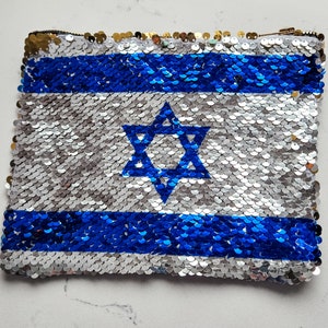 May include: A blue and silver sequin clutch bag with the Israeli flag design. The flag features a blue Star of David on a white background with two blue stripes.