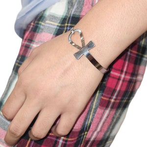 Puede incluir: Pulsera de plata con un diseño de ankh. La pulsera es abierta y ajustable.