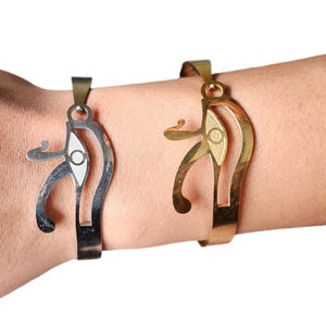 Puede incluir: Dos pulseras de oro y plata con un diseño de ojo de Horus. Las pulseras son ajustables y tienen un aspecto simple y elegante.