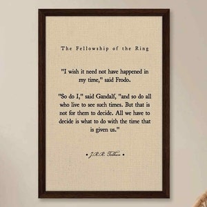 Op de afbeelding: Een ingelijst afdruk van een citaat uit "The Fellowship of the Ring" van J.R.R. Tolkien. Het citaat luidt: "Ik wou dat het niet in mijn tijd hoefde te gebeuren", zei Frodo. "Ik ook", zei Gandalf, "en iedereen die zulke tijden meemaakt. Maar dat is niet aan hen om te beslissen. Alles wat we moeten beslissen is wat we doen met de tijd die ons gegeven is."