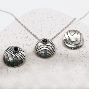 May include: A silver necklace and earrings set with black gemstone accents. The pendant and earrings feature a textured, wavy design.