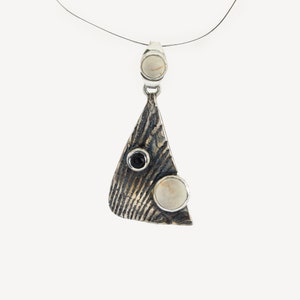May include: A silver pendant with a textured triangular shape, featuring three stones: two white and one black.
