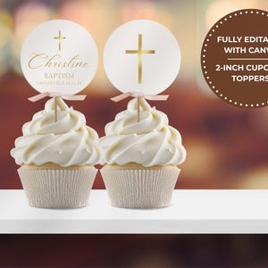 Könnte beinhalten: Zwei Cupcakes mit weißem Zuckerguss und dekorativen Toppern. Die Topper sind rund mit einem goldenen Kreuz und dem Namen "Christine" in goldener Schrift. Der Text "Baptism Greenville 11.11.24" befindet sich ebenfalls auf dem Topper. Ein brauner Kreis mit Text befindet sich im Hintergrund.