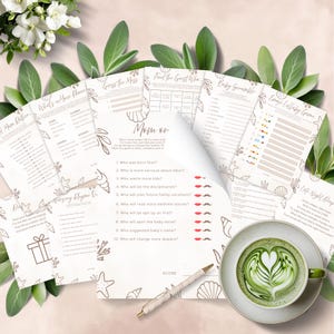 Puede incluir: Un conjunto de hojas de juegos para baby shower de color beige con ilustraciones de conchas marinas y flores. Los juegos incluyen "Mom or", "What's in Mom's Phone" y "Baby Scramble". También se ve una taza de matcha latte con arte latte y un bolígrafo.