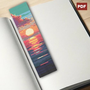 Peut inclure: Marque-page en perles représentant un coucher de soleil. Le design passe du turquoise à l'orange, au rouge et au bleu foncé, avec un soleil sur l'eau et des lignes horizontales. Le marque-page est dans un livre ouvert. Le design ressemble à une image pixélisée.