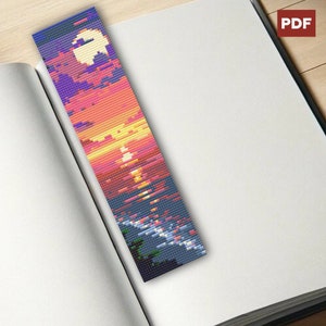 Könnte beinhalten: Ein Perlen-Lesezeichen mit einer Sonnenuntergangsszene über einem Gewässer. Das Lesezeichen besteht aus bunten Perlen und zeigt einen leuchtend orangefarbenen, gelben und rosafarbenen Sonnenuntergang mit blauem Himmel und Wasser. Im Vordergrund befinden sich zwei kleine grüne Bäume.