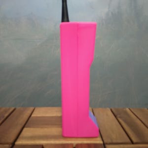 May include: A bright pink, rectangular device with a black antenna. The device has a small, blue accent on the bottom. The object is set on a wooden surface.