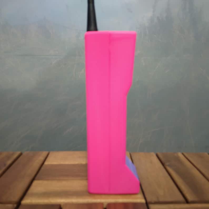 May include: A bright pink, rectangular device with a black antenna. The device has a small, blue accent on the bottom. The object is set on a wooden surface.