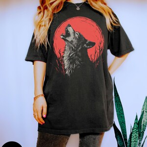 May include: A black t-shirt with a graphic of a wolf howling at a red moon. The wolf is in a black and white silhouette.