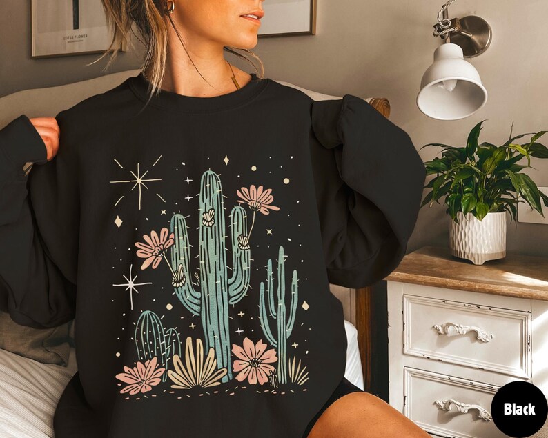 May include: Black sweatshirt with a graphic print of a cactus and flowers. The cactus is green and the flowers are pink and white.