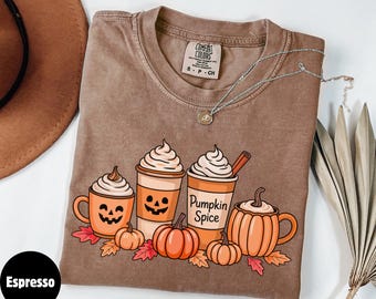 May include: Espresso-colored t-shirt featuring a fall-themed graphic. The design includes pumpkin spice lattes, pumpkins, and autumn leaves. The text "Pumpkin Spice" is visible on one of the cups. The shirt is a Comfort Colors brand.