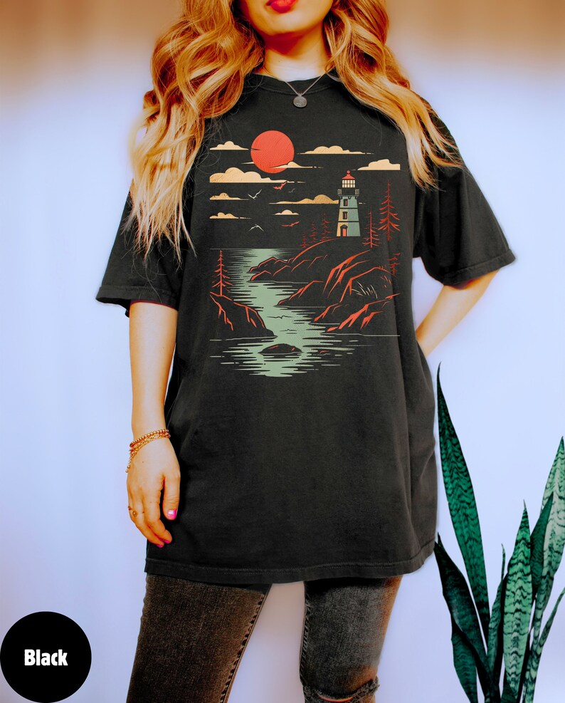 May include: A black t-shirt with a graphic print of a lighthouse on a rocky shore with a red sun setting behind it.