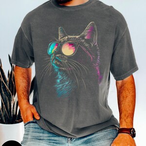 May include: A dark gray t-shirt with a colorful graphic of a cat wearing sunglasses. The cat is looking to the right. The t-shirt is made of a soft, comfortable material.