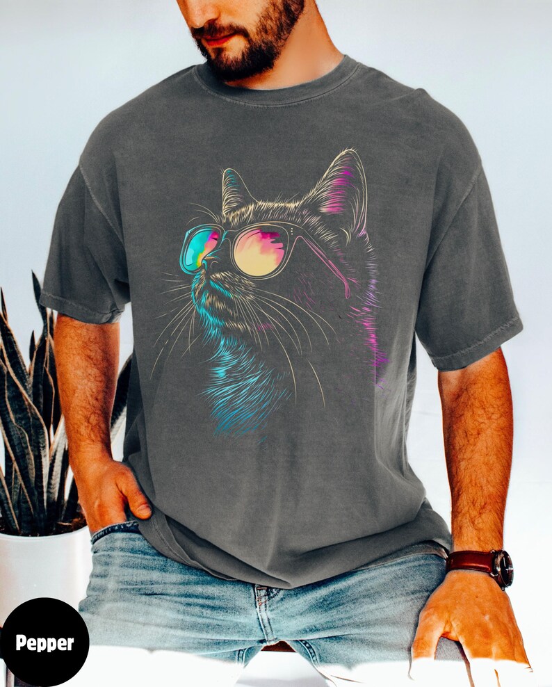 May include: A dark gray t-shirt with a colorful graphic of a cat wearing sunglasses. The cat is looking to the right. The t-shirt is made of a soft, comfortable material.