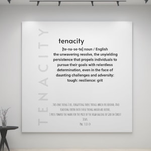 May include: A white wall with a black frame displaying a definition of the word "tenacity" in a gallery setting. The definition is: "[te-na-se-te] noun / English the unwavering resolve, the unyielding persistence that propels individuals to pursue their goals with relentless determination, even in the face of daunting challenges and adversity. tough: resilience: grit"