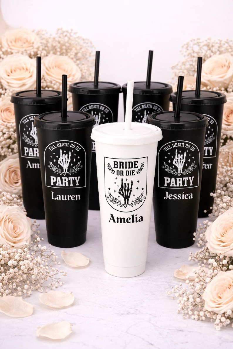 May include: A collection of black and white tumblers with lids and straws. The black tumblers have the text "TILL DEATH DO US PARTY" and names. The white tumbler has the text "BRIDE OR DIE" and a name. The tumblers are surrounded by flowers.
