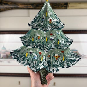 Op de afbeelding: Een keramische kerstboom met een groene basis en witte accenten. De boom is versierd met kleurrijke ornamenten en heeft een textuur. De boom is ongeveer 25 cm hoog.