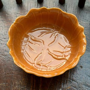 May include: A small, brown ceramic bowl with a scalloped edge and a leaf design. The bowl is glazed and has a shiny finish.