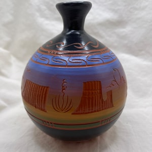 Puede incluir: Un pequeño jarrón de cerámica pintado a mano con base negra, una banda azul y morada y una banda marrón con un diseño de paisaje desértico.