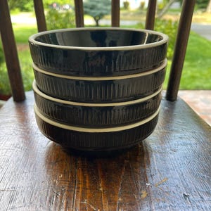 May include: A set of three black ceramic bowls with white rims. The bowls are stacked on top of each other. The bowls have a textured, ribbed design.