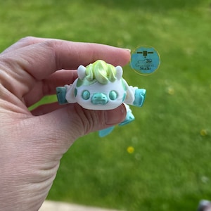 May include: A 3D-printed, white and mint-green cartoon character with a light green tuft of hair. The figure has outstretched arms and a smiling face. The logo for "3D Generation Studio" is visible in the background.