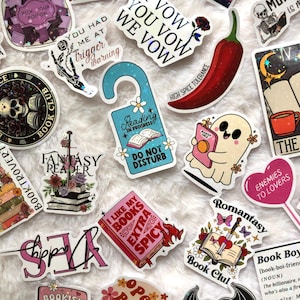 May include: A collection of colorful stickers with various designs and text. Themes include books, reading, and fantasy. Some stickers feature phrases like "Reading in Progress" and "I Like My Books Extra Spicy."