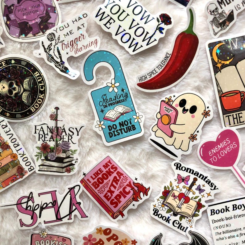 May include: A collection of colorful stickers with various designs and text. Themes include books, reading, and fantasy. Some stickers feature phrases like "Reading in Progress" and "I Like My Books Extra Spicy."