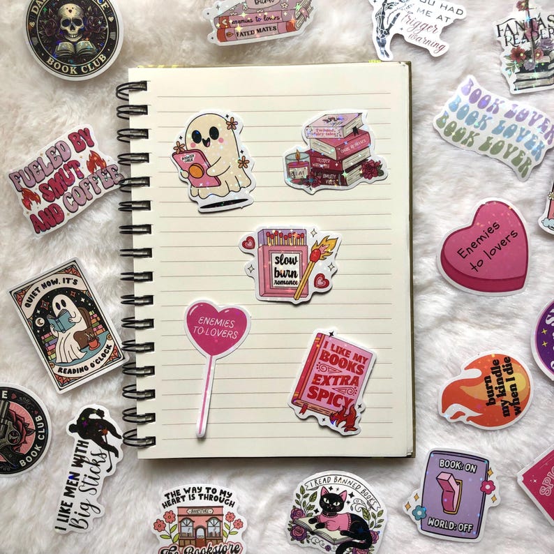 May include: A collection of colorful stickers with book-related themes. Designs include a ghost reading, stacks of books, a matchbook with the text "slow burn romance," and a heart-shaped lollipop that says "Enemies to lovers." Other stickers say "Book Club."