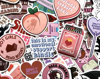 Op de afbeelding: Een verzameling roze en paarse stickers met boekthema's. De stickers bevatten zinnen als "emotionele steun kindle", "langzaam brandende boekenclub", "hete meiden lezen boeken" en "pittige lezer".