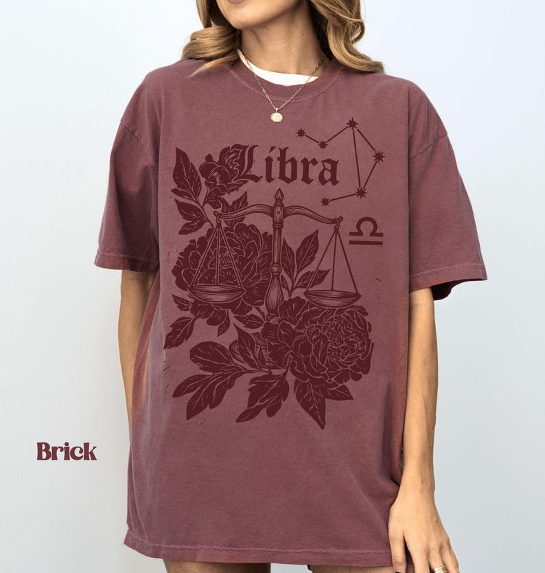 Op de afbeelding: Baksteenkleurig T-shirt met een Weegschaal-ontwerp. Het ontwerp bevat het woord "Libra", een weegschaal, bloemelementen en een sterrenbeeld. Het shirt heeft korte mouwen en een ronde hals.