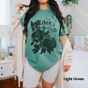 Op de afbeelding: Lichtgroen T-shirt met een Weegschaal sterrenbeeld ontwerp. Het ontwerp bevat het woord "Libra", een weegschaal en bloemelementen in zwart. Het shirt is lichtgroen en heeft een relaxte pasvorm.