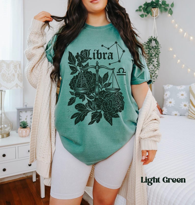 Op de afbeelding: Lichtgroen T-shirt met een Weegschaal sterrenbeeld ontwerp. Het ontwerp bevat het woord "Libra", een weegschaal en bloemelementen in zwart. Het shirt is lichtgroen en heeft een relaxte pasvorm.